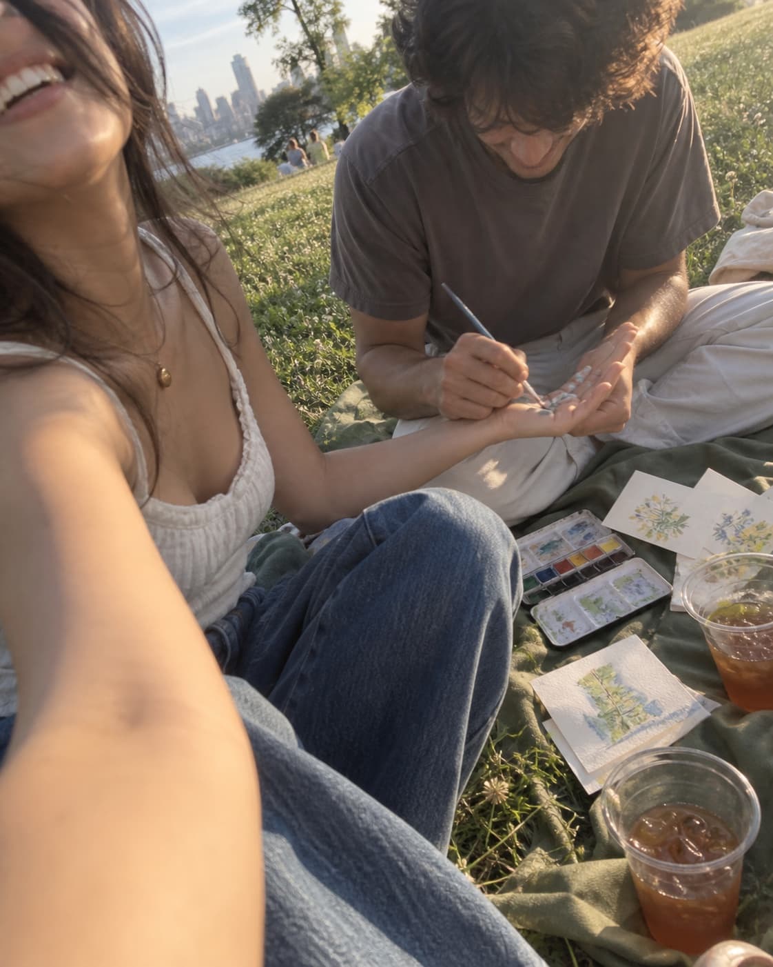Two people writing and drawing on a blanket outdoors, drinks beside them